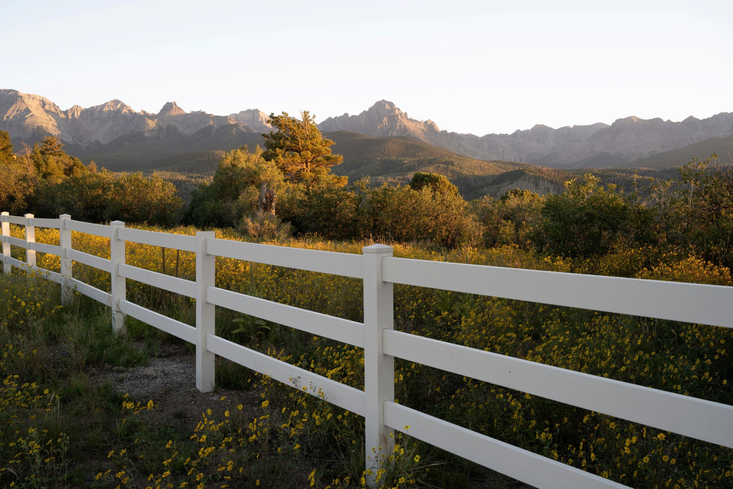 A white fence in a field with mountains in the background