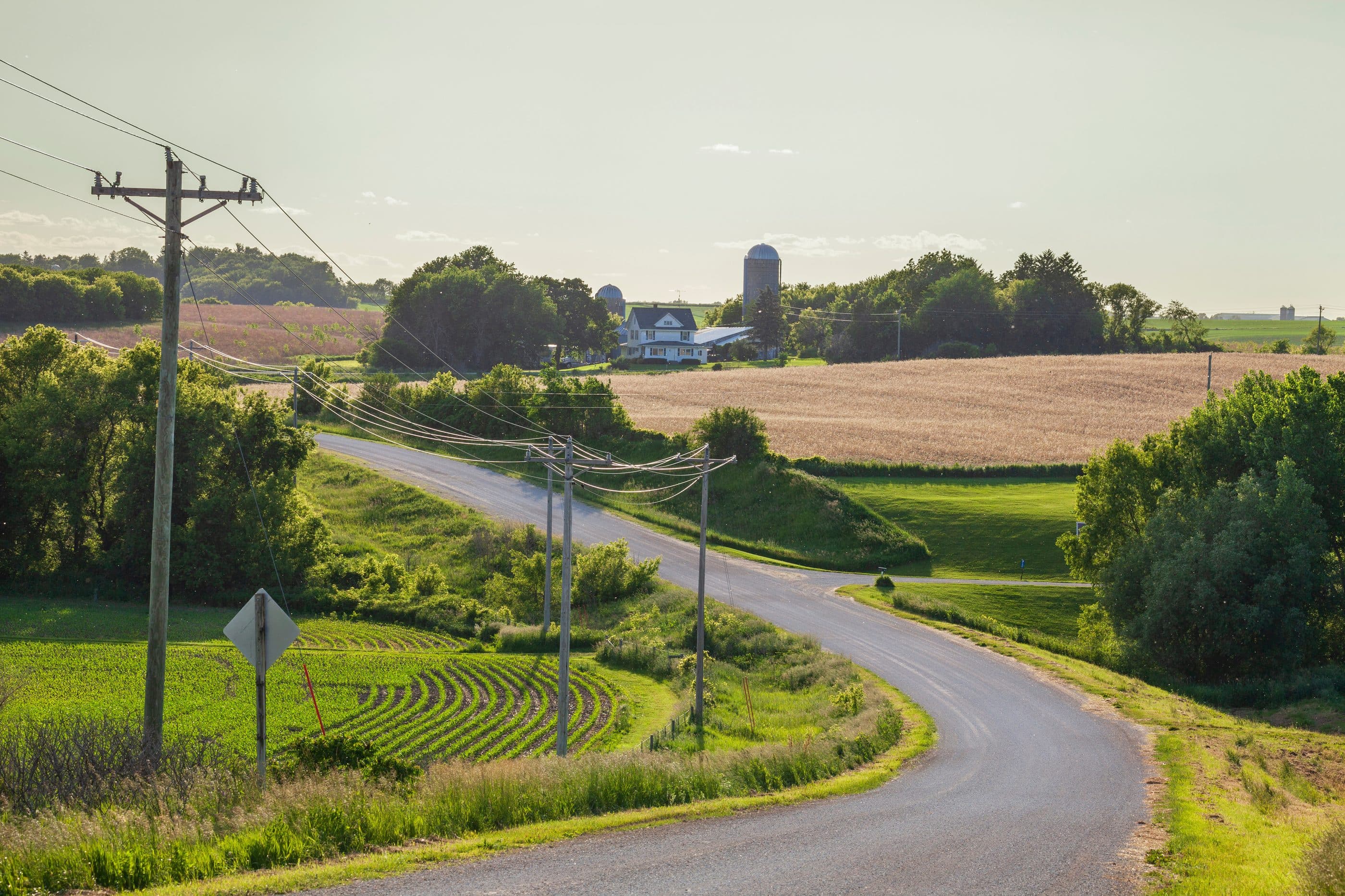 A country road winding past a farm and a single utility pole